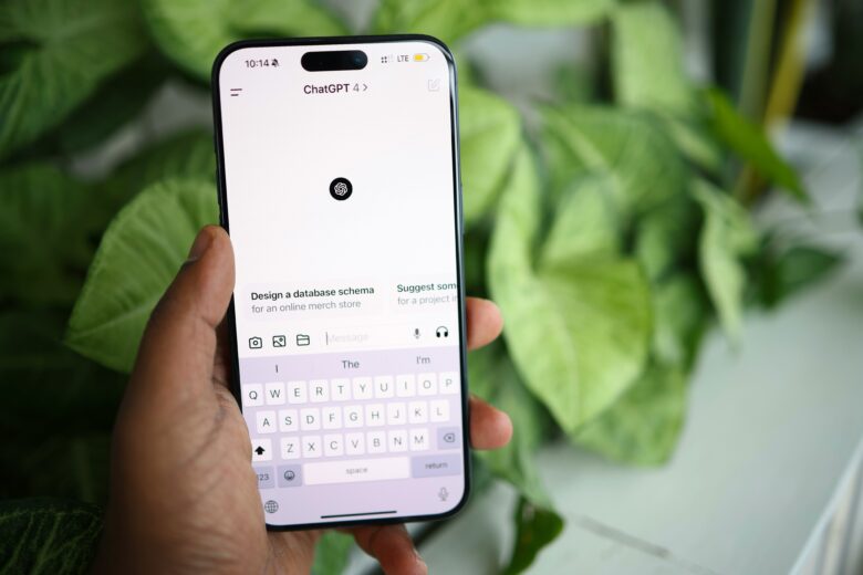 Mano sujetando un iPhone con la aplicación ChatGPT abierta y teclado visible, con plantas de fondo