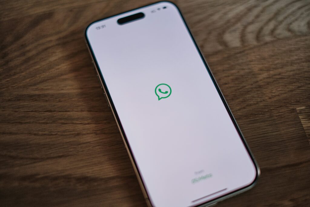 iPhone con pantalla de carga de WhatsApp apoyado sobre mesa de madera