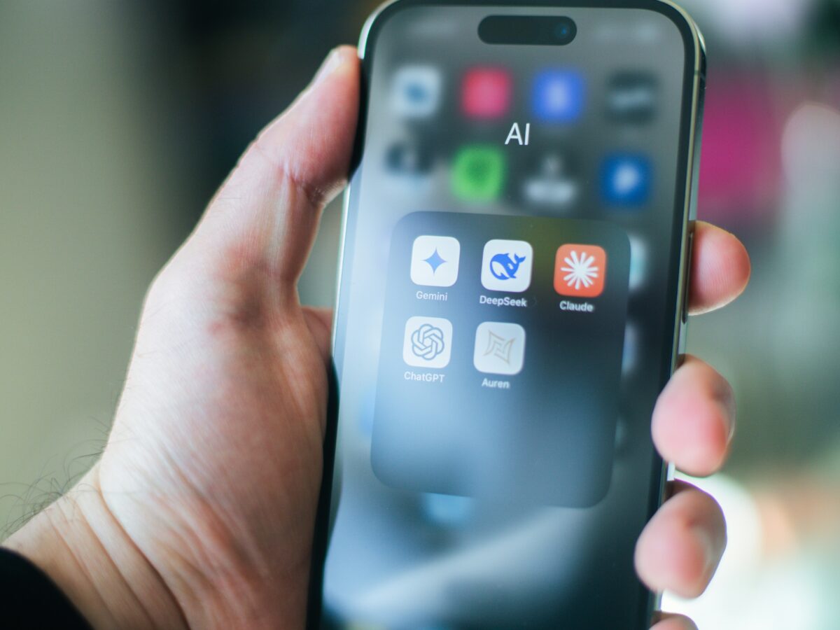 Persona sosteniendo un smartphone con una carpeta de aplicaciones de inteligencia artificial que incluye ChatGPT, Gemini, Claude y DeepSeek.