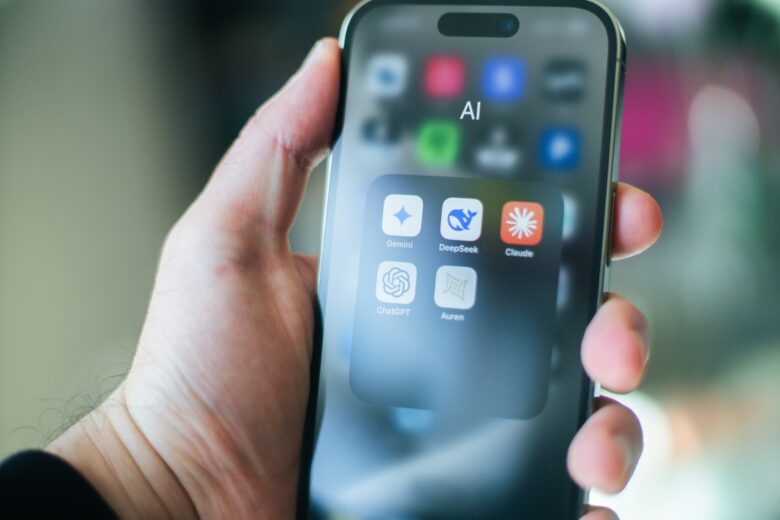 Persona sosteniendo un smartphone con una carpeta de aplicaciones de inteligencia artificial que incluye ChatGPT, Gemini, Claude y DeepSeek.